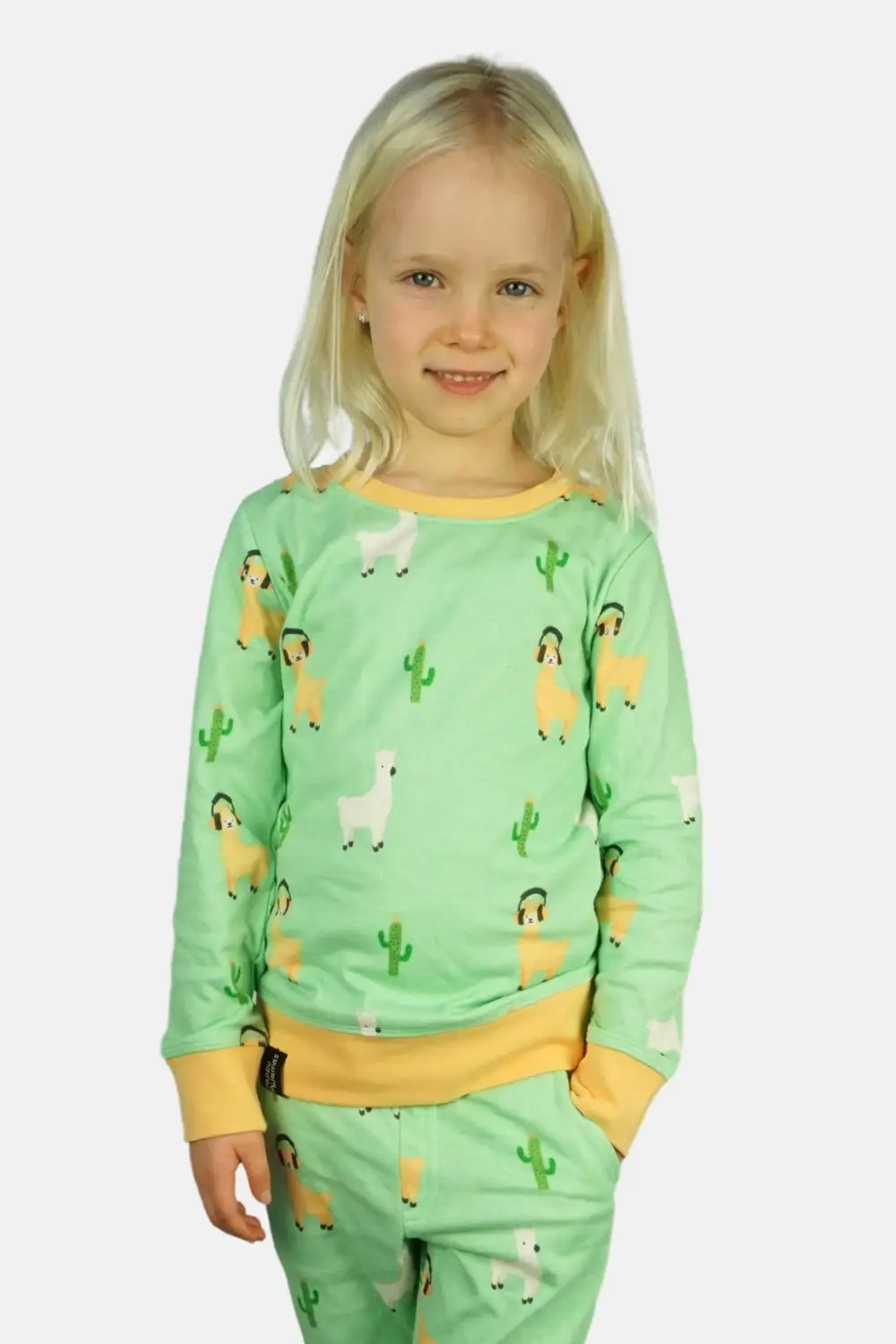 Vooraanzicht kinderpyjama met alpaca's. Meisje heeft haar hand in de broekzak.