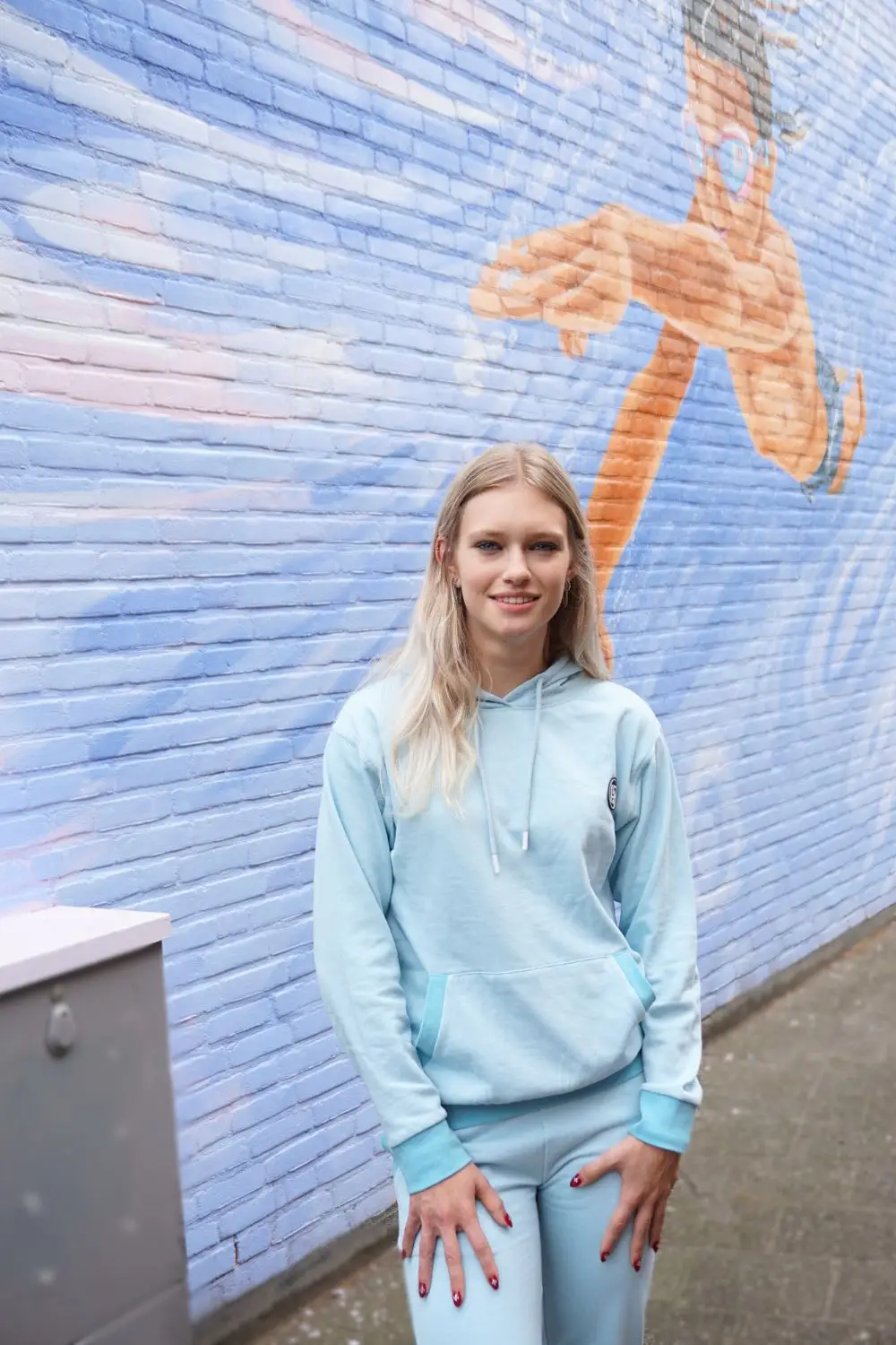 Op straat bij een muurschildering in een blauwe joggingpak.